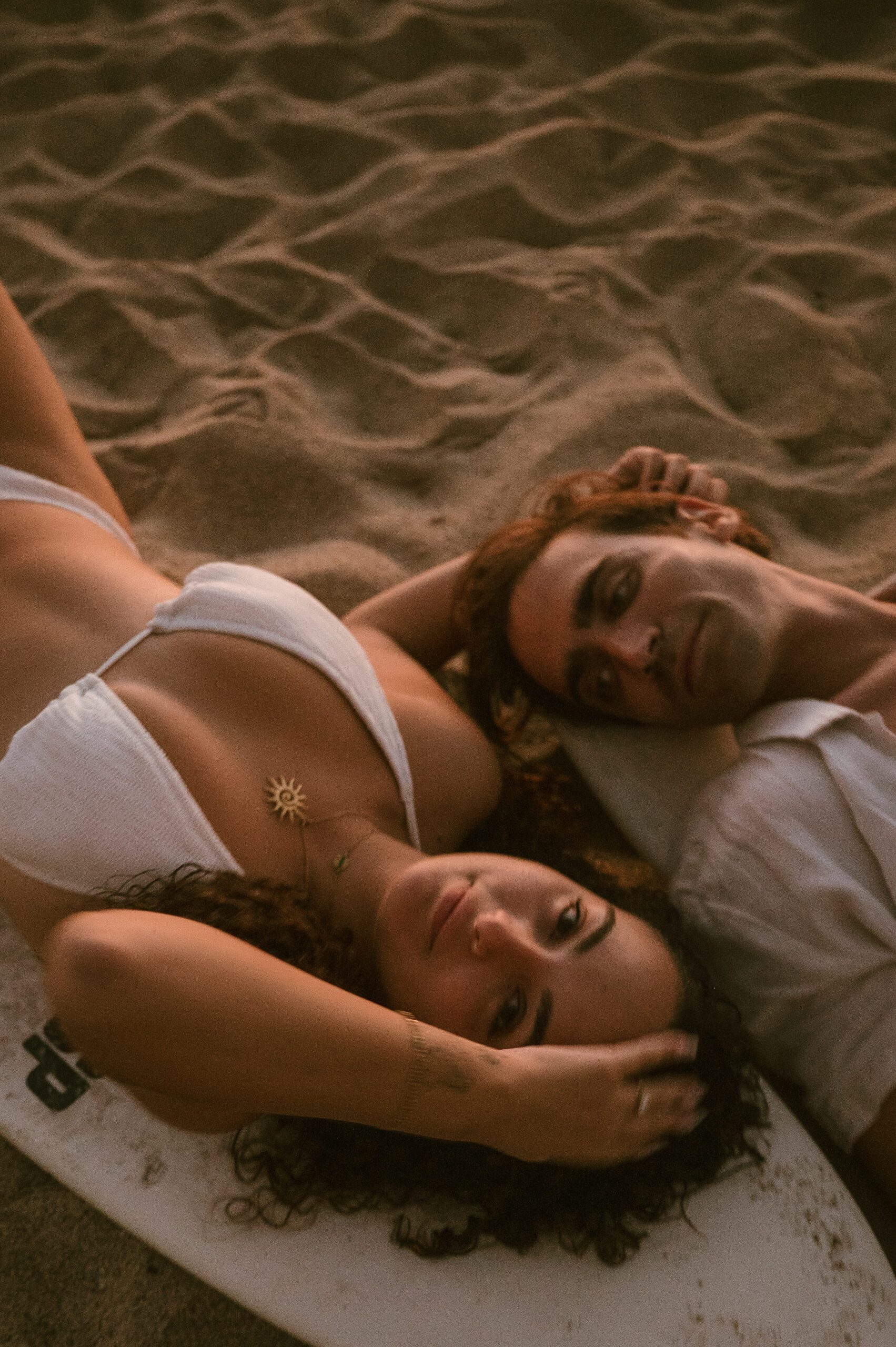 Newly engaged couple lay on surf board on beach in love