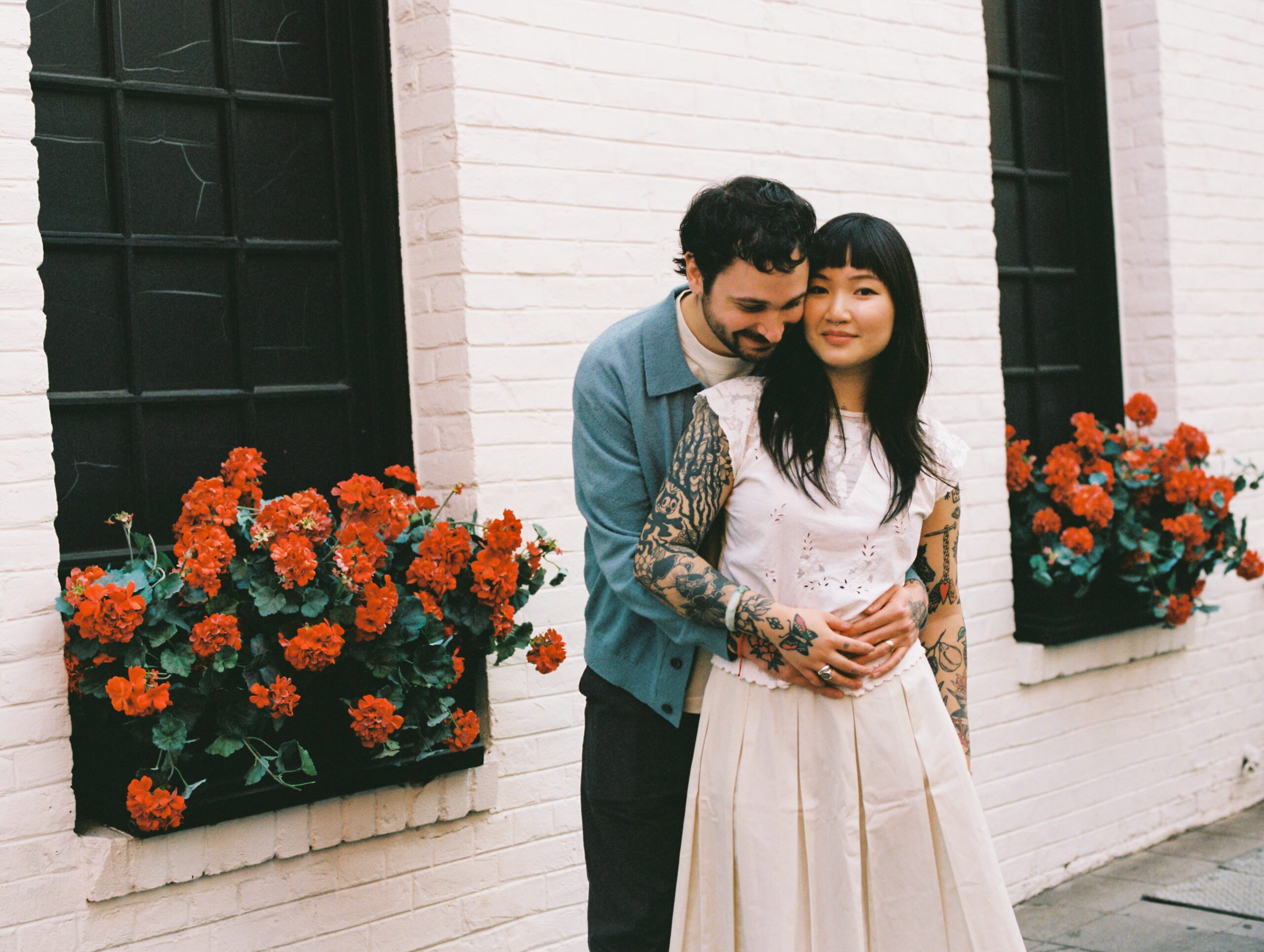 Cute candid photo of married husband and wife cuddling in front of red flowers in Pasadena taken by wedding photographer LA